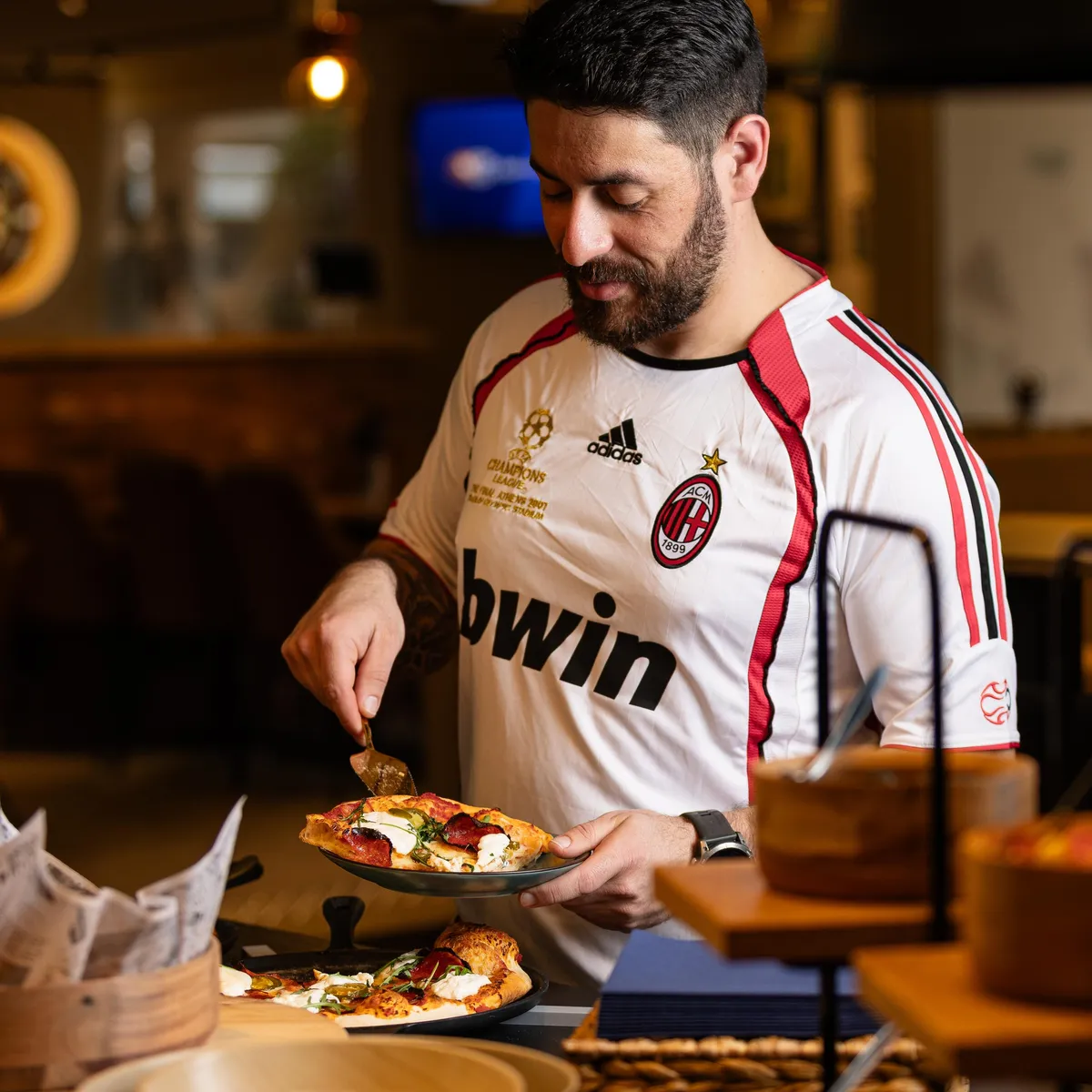 Un homme en t-shirt de football prépare une pizza dans un restaurant