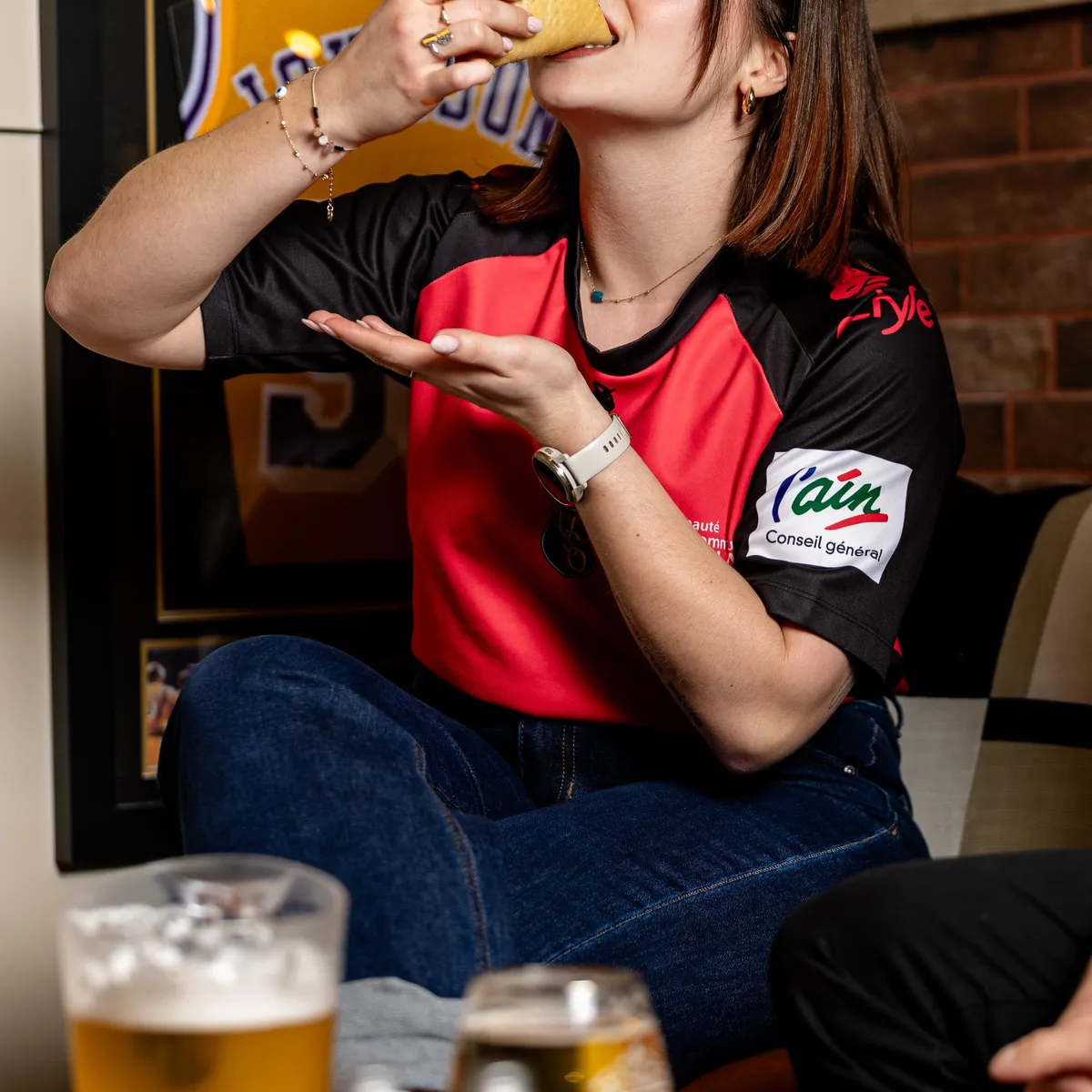 Une personne mange un sandwich en tenant un verre de bière devant une télévision