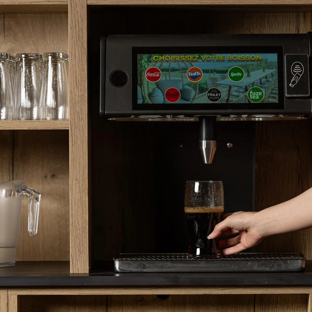 Une personne utilise un distributeur de boissons pour sélectionner une boisson, avec des verres à proximité