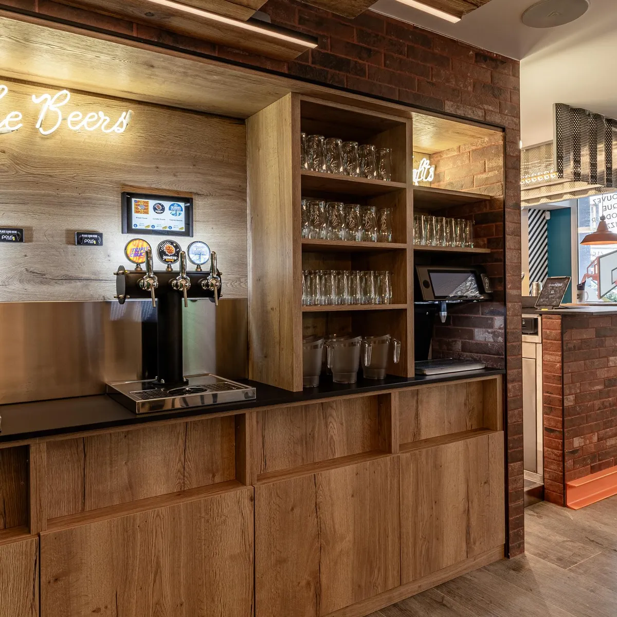 Un bar à bières avec plusieurs pompes à bière, des étagères à verres et des écrans affichant des informations, dans un intérieur moderne avec des éléments en bois et en brique