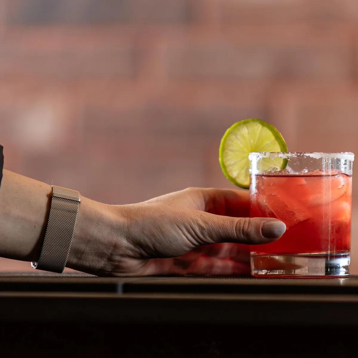 Une main tenant un verre contenant un liquide rouge avec des glaçons et une tranche de citron vert sur le bord