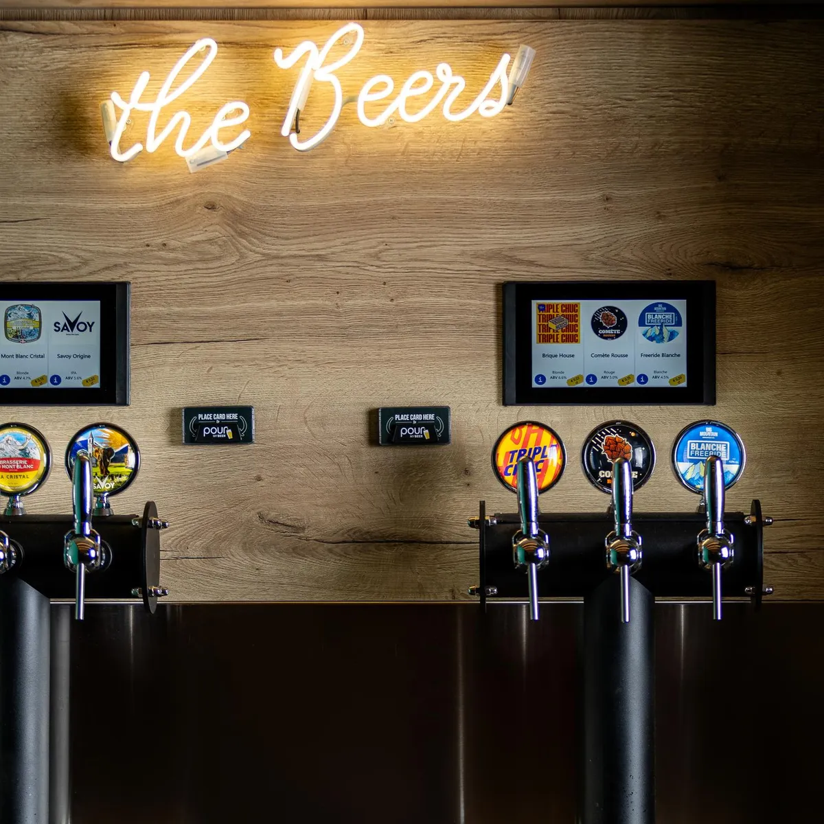 Un bar à bières avec six pompes à bière et des écrans affichant les types de bières disponibles