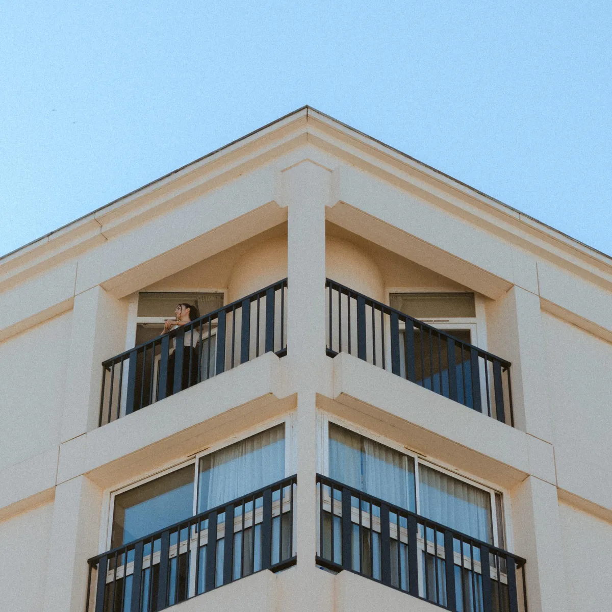 Personne debout sur un balcon au coin d'un immeuble beige avec des balustrades noires