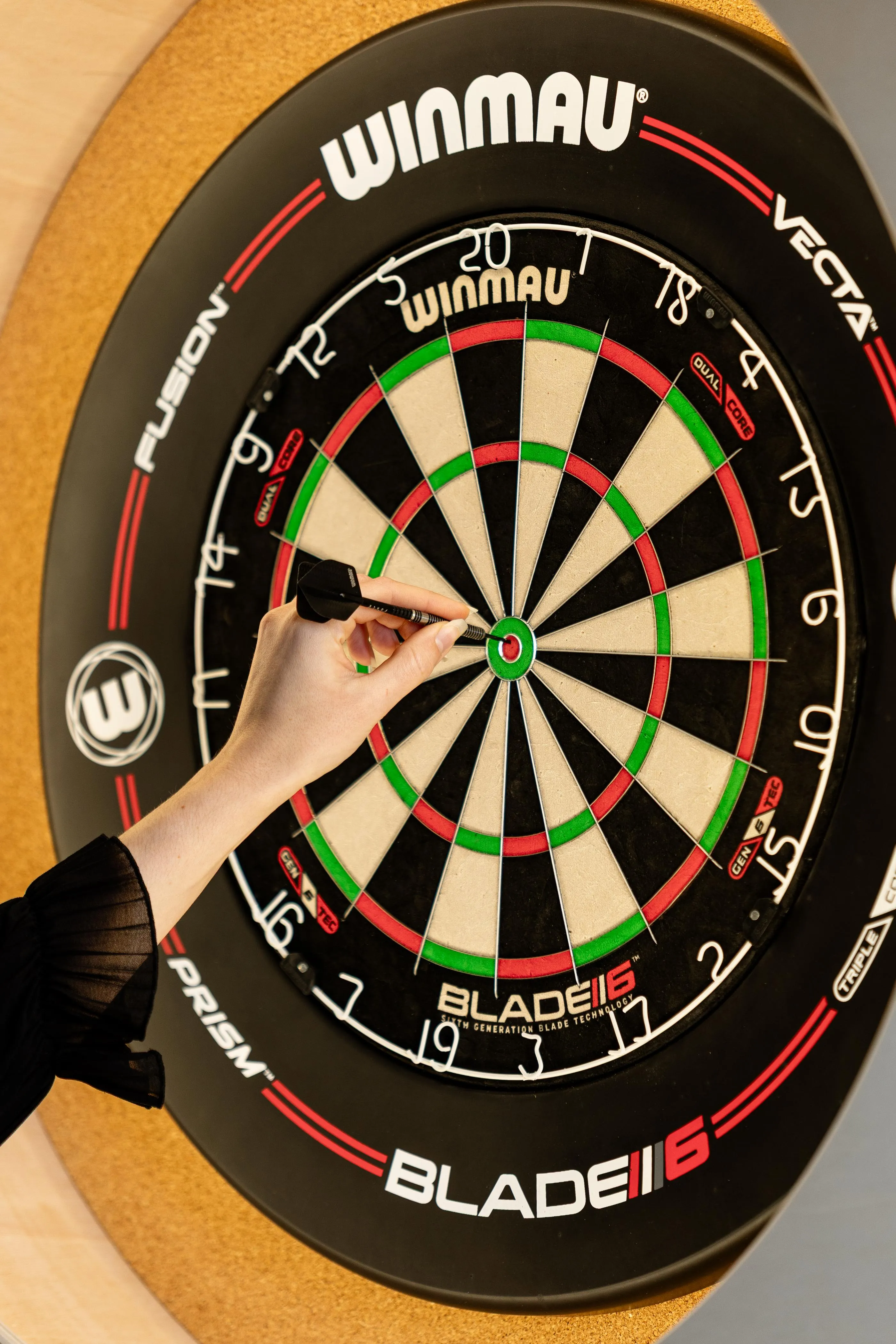 Une main tient un fléchette pointée vers le centre d'une cible de fléchettes Winmau Blade6