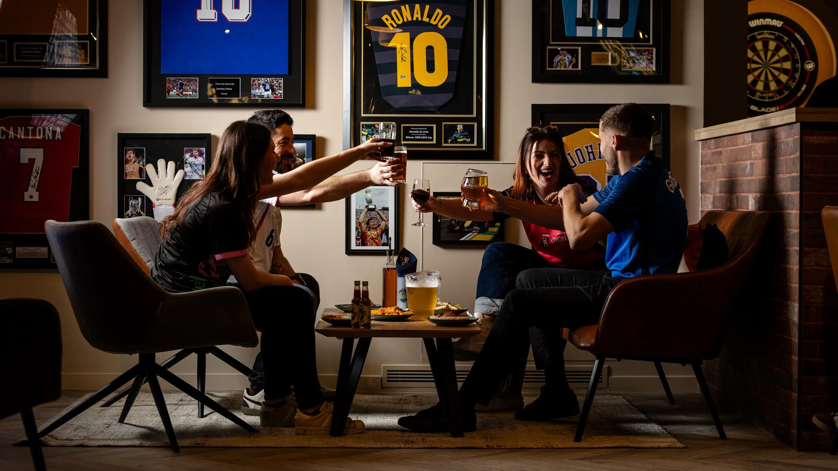 Quatre personnes assises autour d'une table avec des boissons et de la nourriture, dans un cadre décoré de posters sportifs