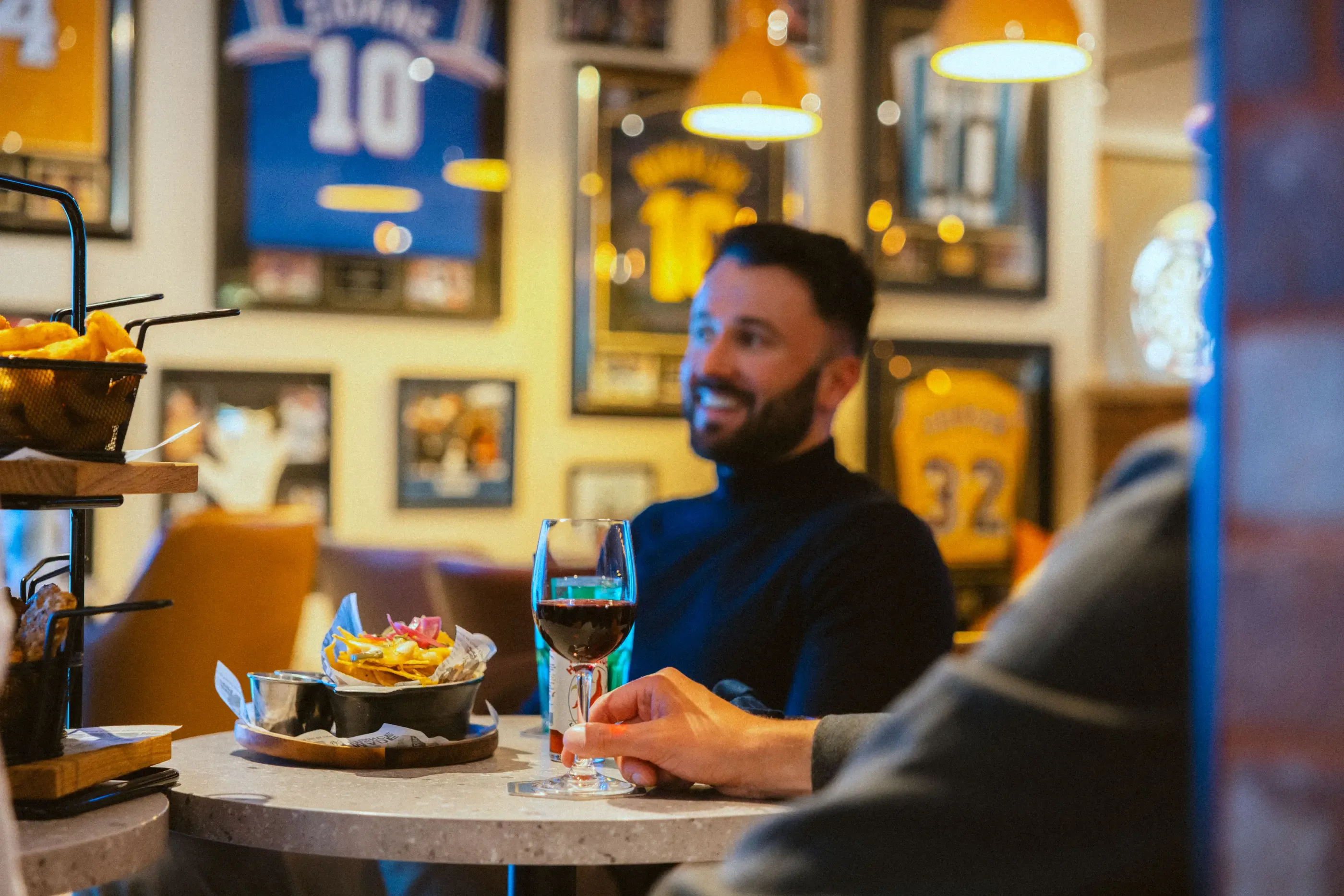 Un homme assis à une table avec un verre de vin et un bol de nourriture dans un restaurant décoré de posters sportifs