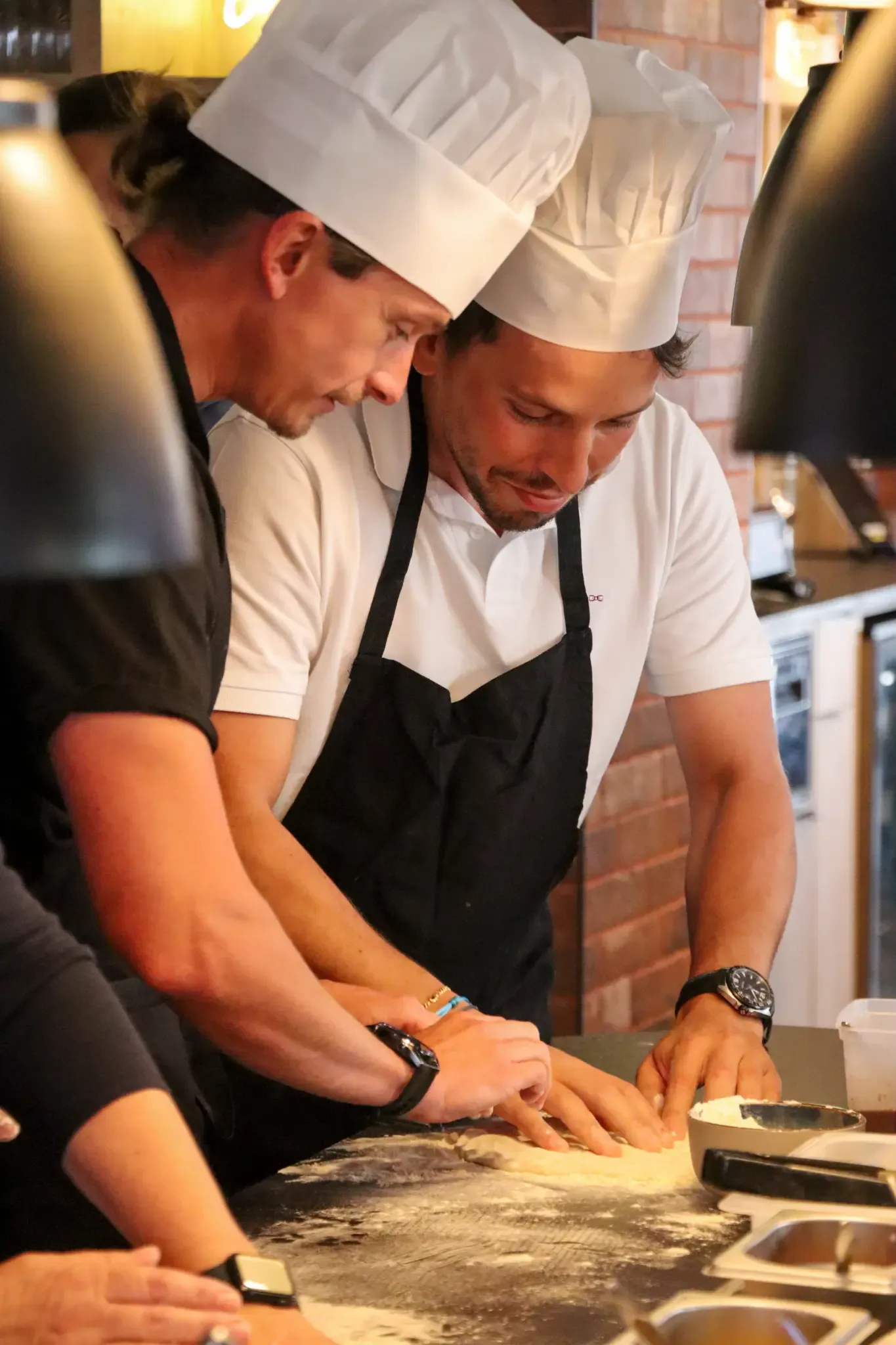Deux personnes portant des toques de chef et des tabliers cuisinent ensemble dans une cuisine professionnelle