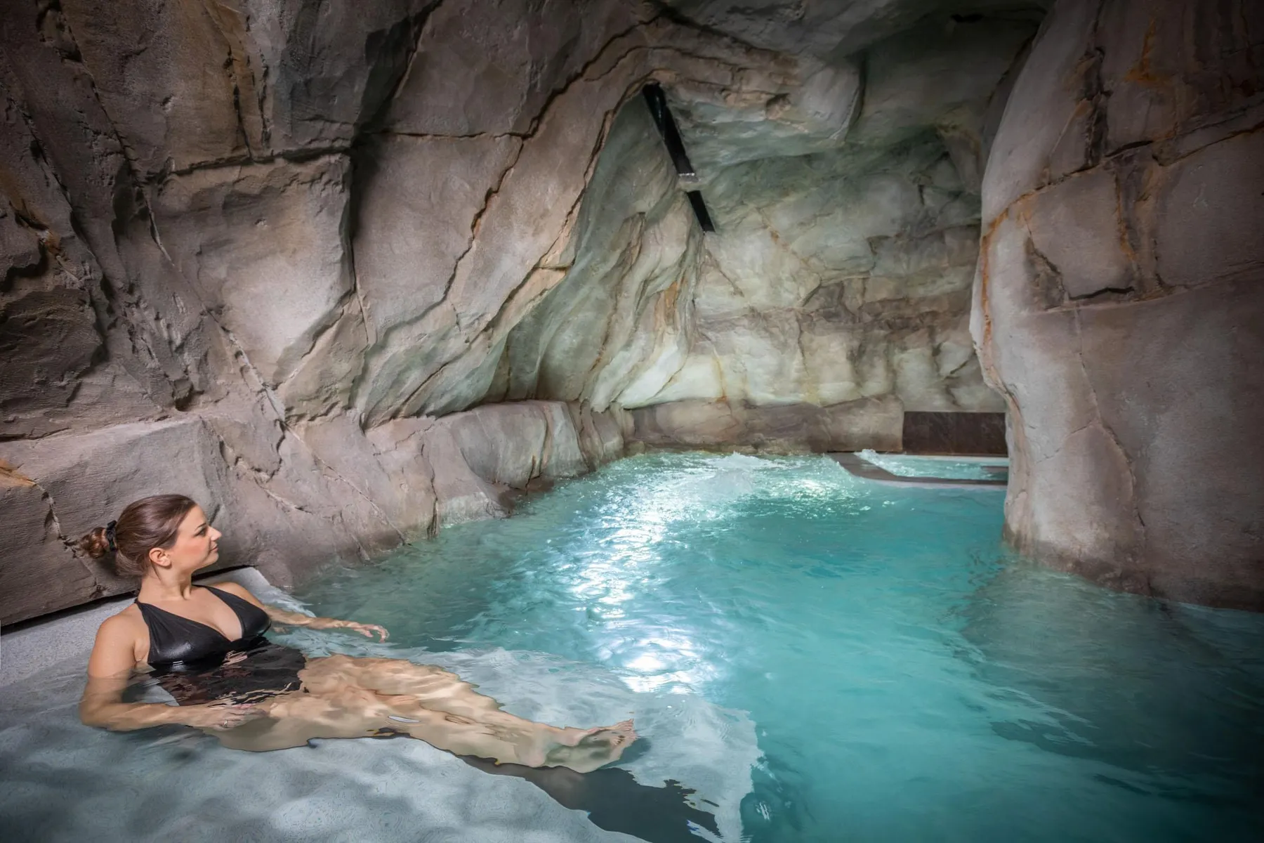 Une personne est allongée dans une piscine d'eau bleue située dans une grotte artificielle aux parois rocheuses