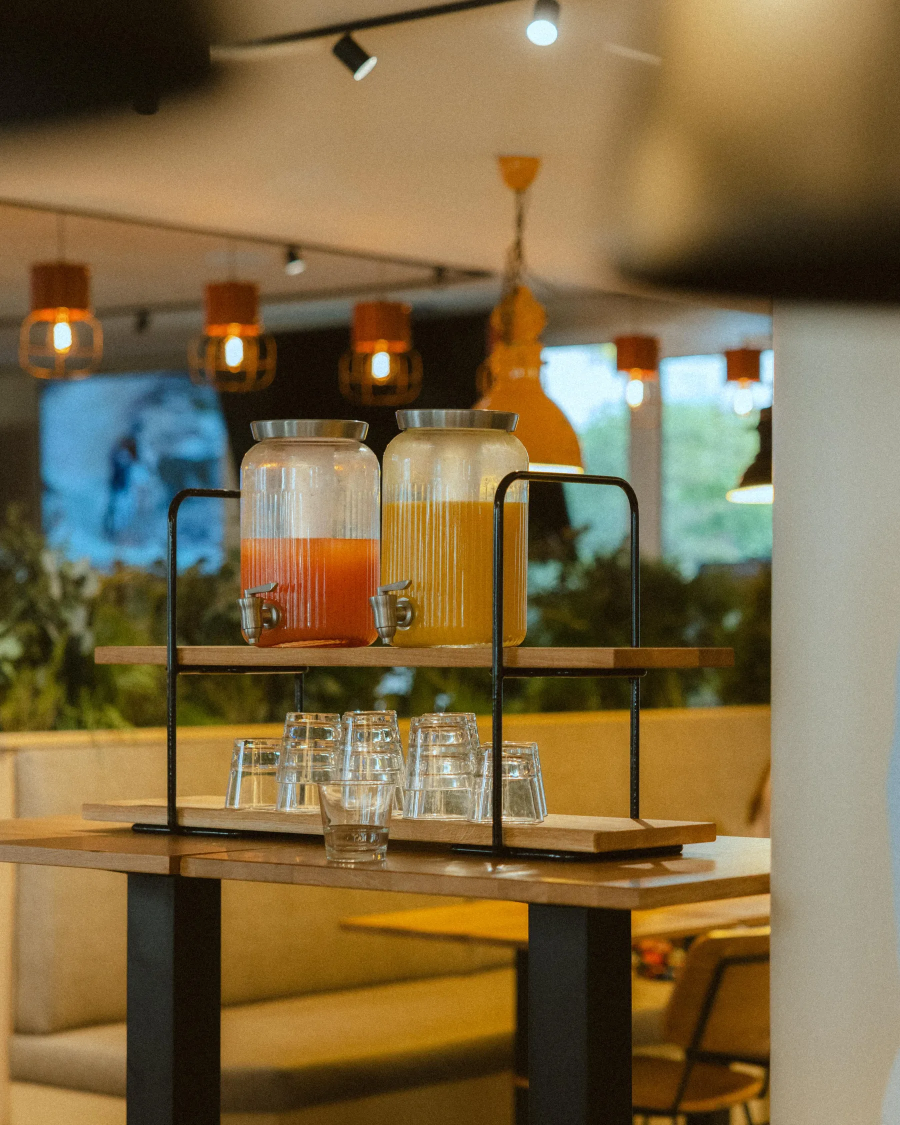 Deux jarres de boissons colorées sur une étagère avec des verres en dessous dans un cadre intérieur lumineux
