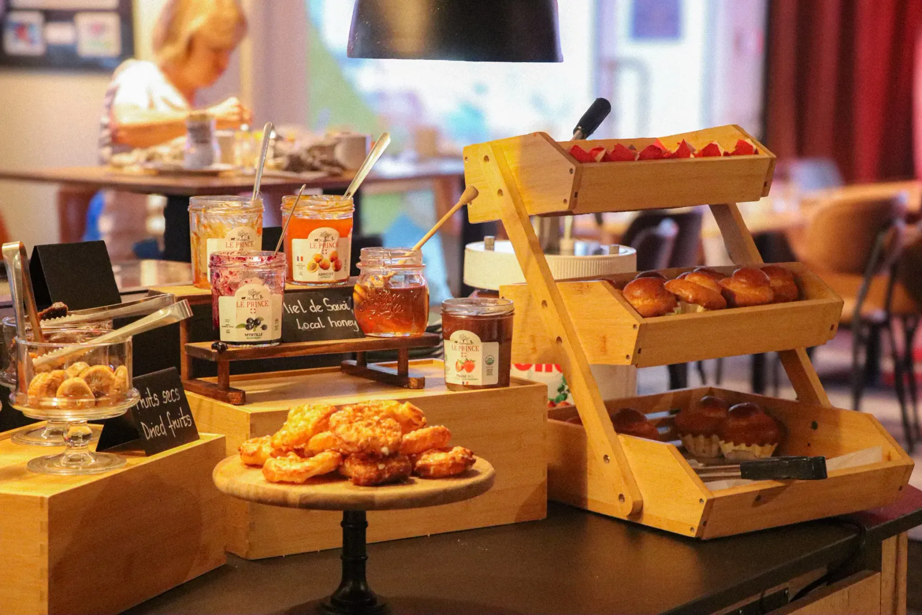 Un comptoir de café avec des pâtisseries, des pots de confiture et des fruits secs exposés sur des étagères en bois