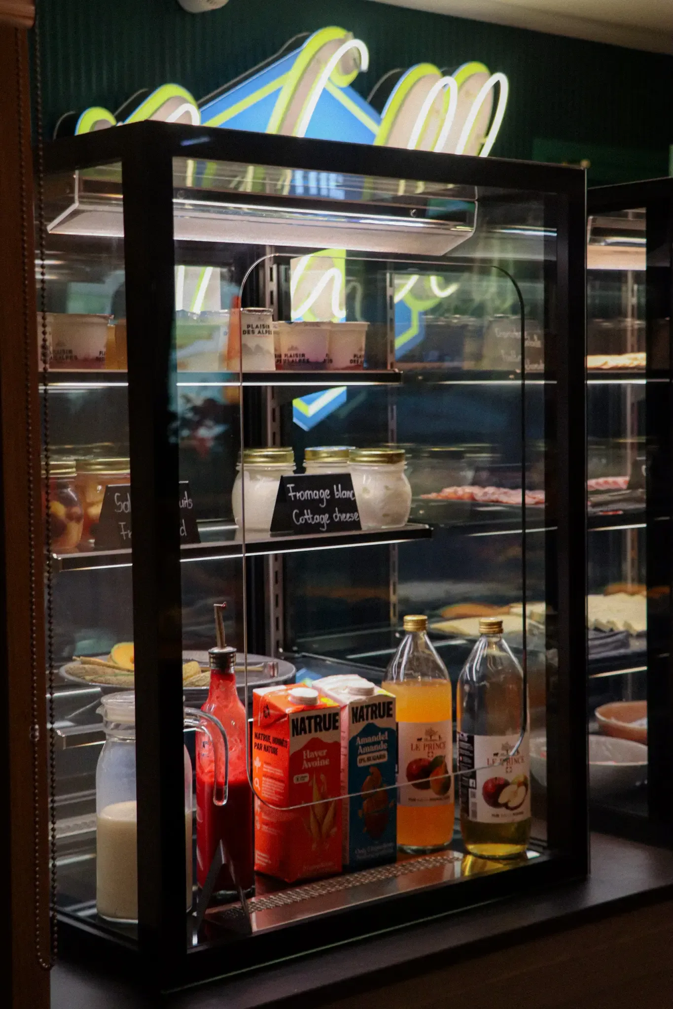 Présentation de produits alimentaires dans une vitrine réfrigérée avec des étagères contenant des boissons, des condiments et des fromages
