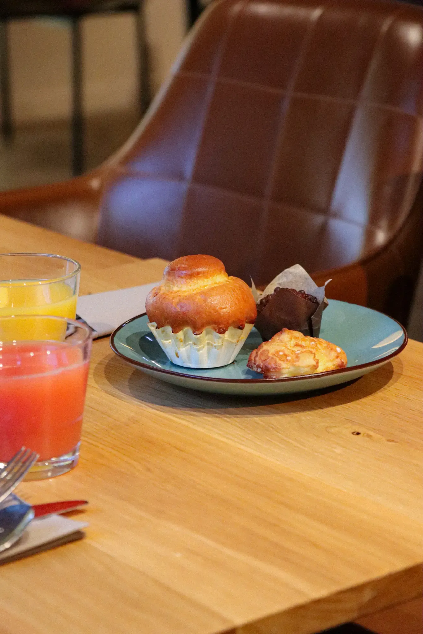 A tray with a muffin, a pastry, and a small chocolate cake on a wooden table, accompanied by two glasses of juice.