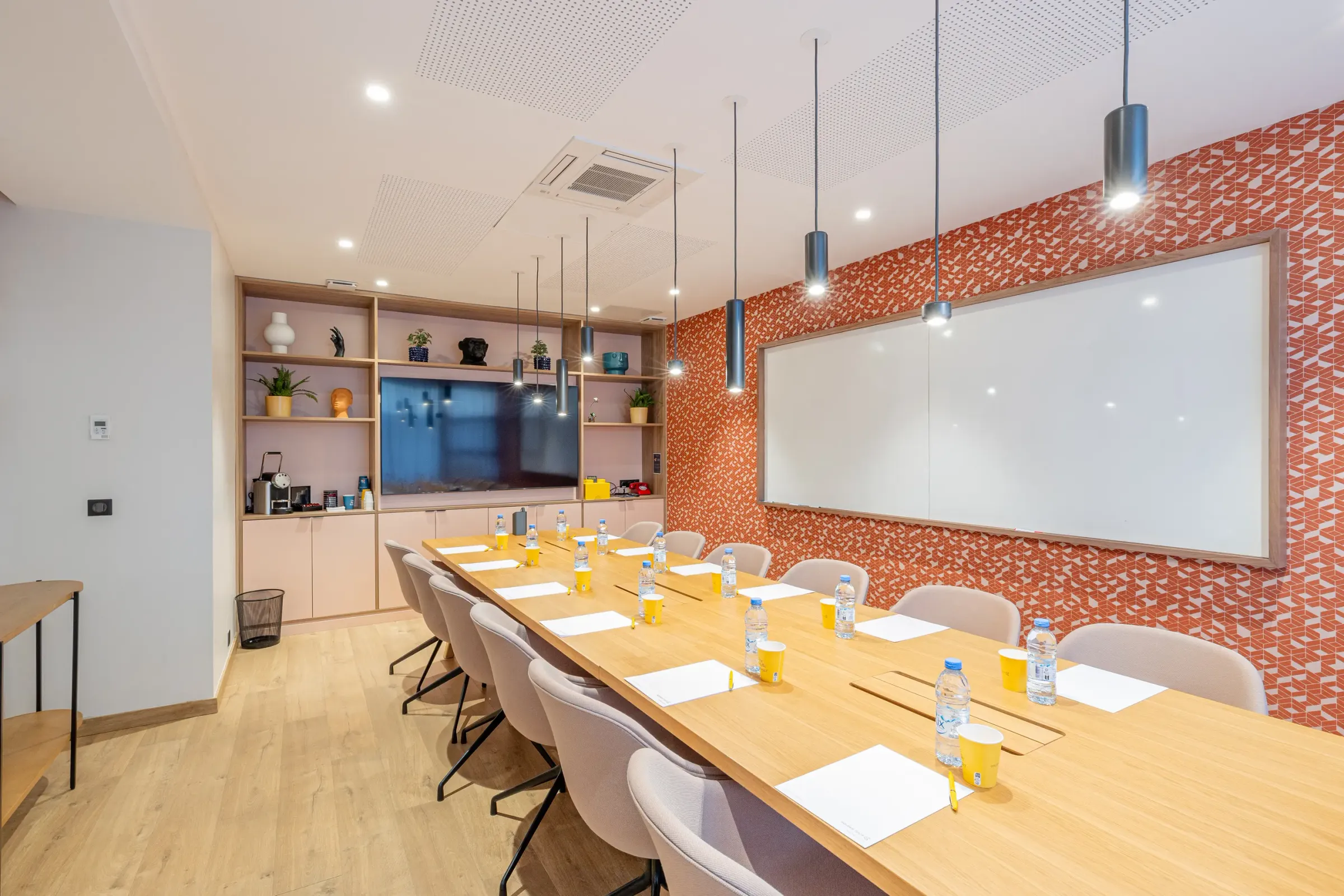 Salle de réunion avec une table en bois, des chaises, des bouteilles d'eau, des blocs-notes et un écran mural