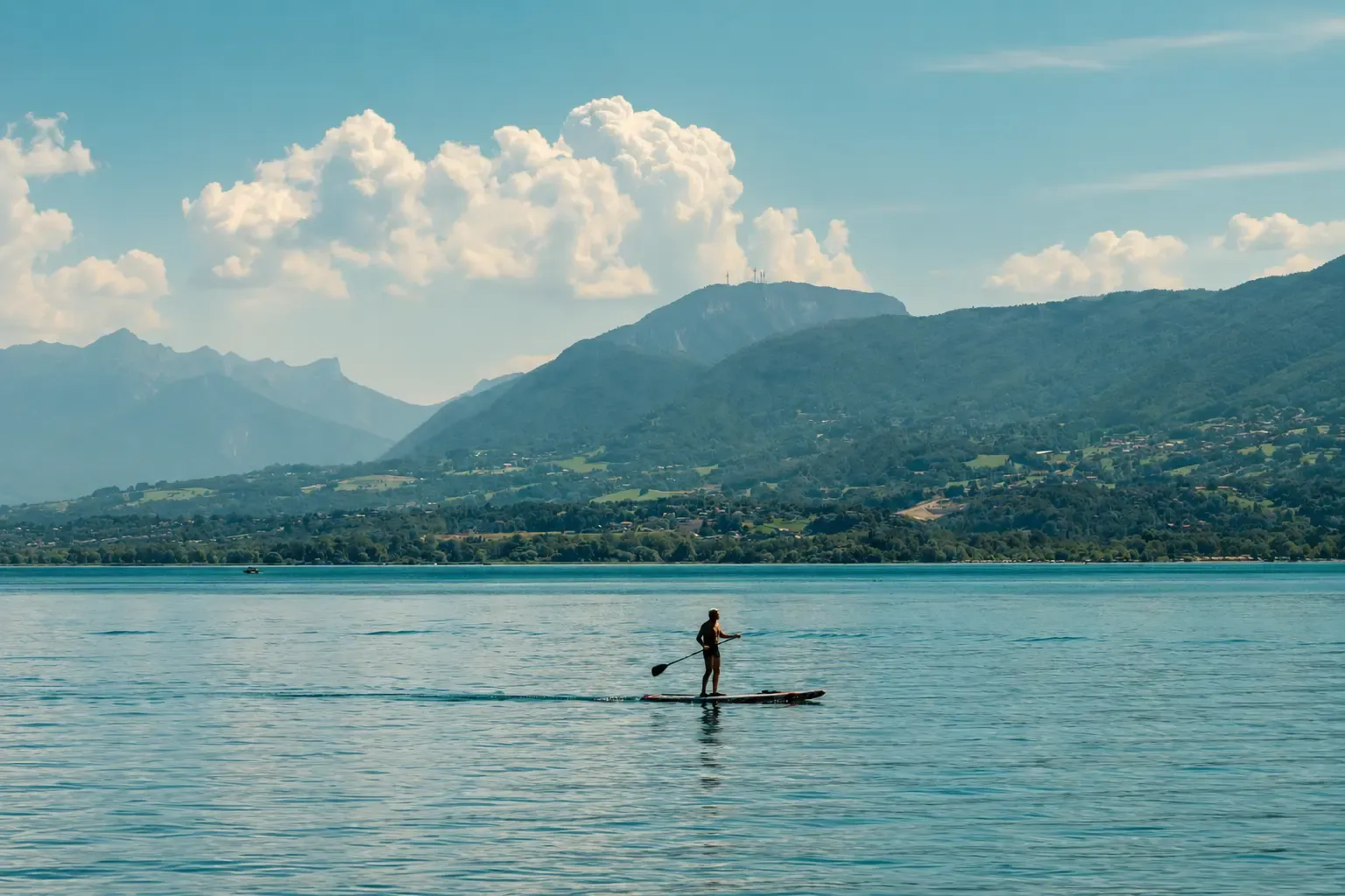 Une personne fait du paddle sur un lac avec des montagnes en arrière-plan