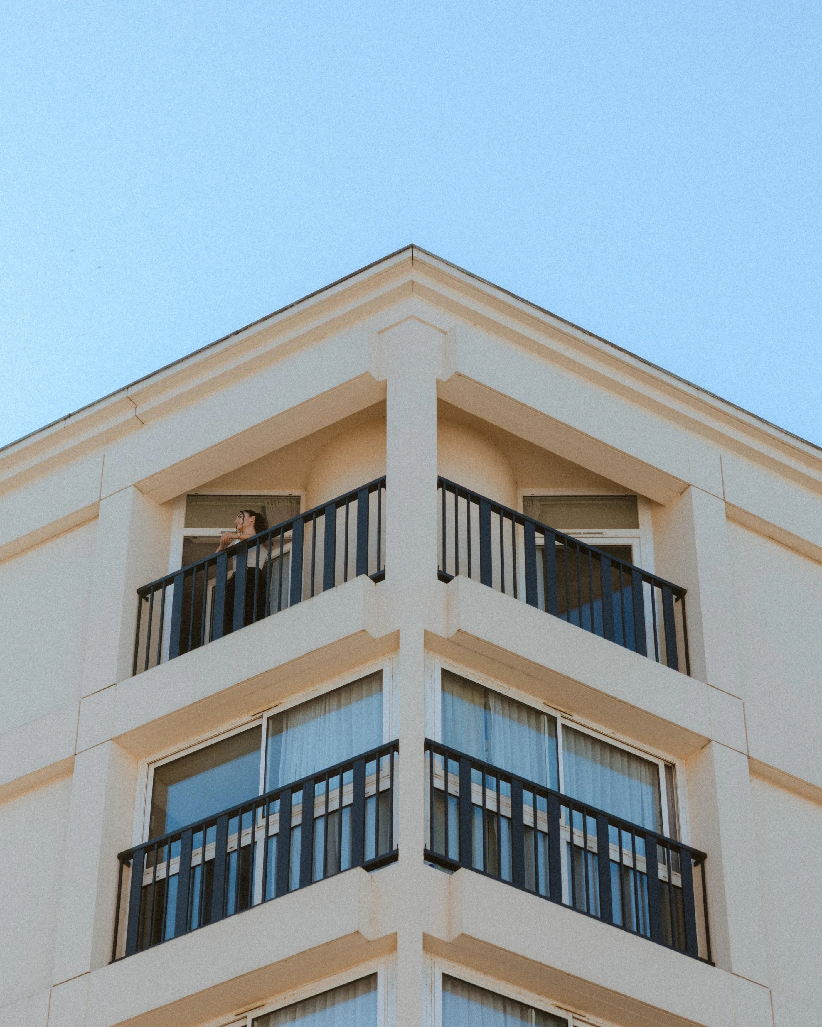 Personne debout sur un balcon au coin d'un immeuble beige avec des balustrades noires